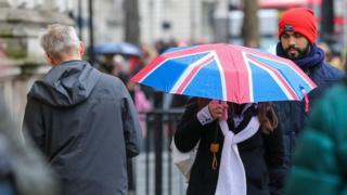 A woman shelters from the rain beneath a Union Jack umbrella during rainfall in central London.