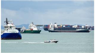 A boat sails past shipping vessels anchored off at the straits in Singapore on 11 August 2014.