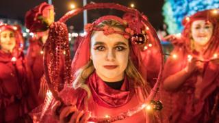 Young woman wearing a red Halloween costume with white face paint and cat-like contact lenses