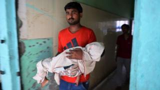 Hombre con niño en brazos saliendo del hospital Baba Raghav Das Hospital en Gorakhpur, en el estado de Uttar Pradesh en el Norte de la INdia, donde murieron 60 menores en 6 días.