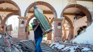 Un hombre cargando la estatua de San Judas entre los escombros de la parroquia de la Inmaculada Concepción