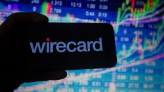 Wirecard logo on phone against stock market charts.