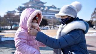 A woman helps her daughter seen wearing a face mask in Pyongyang