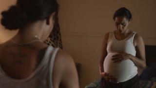 A pregnant Indigenous Australian woman looks into a mirror holding her stomach in this still from a TV ad campaign
