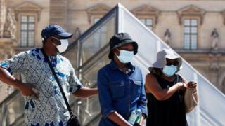 People wearing protective masks walk near the Louvre Museum in Paris