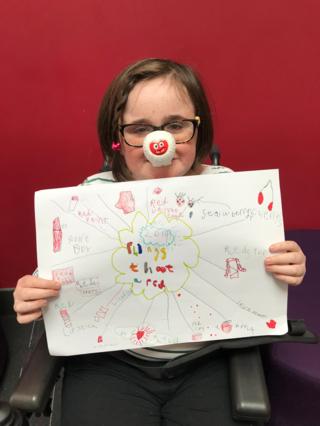 a young girl holding up a poster for red nose day