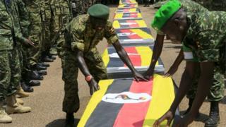 Uganda army soldiers lay national flags on the caskets carrying the remains of Ugandan soldiers who were killed in Somalia this week, at a military airbase in Entebbe on 3 September 2015