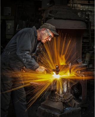 A blacksmith strikes hot metal with sparks flying