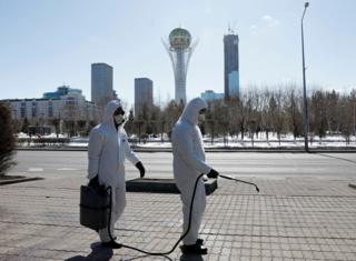 люди в костюмах химзащиты опрыскивают улицы