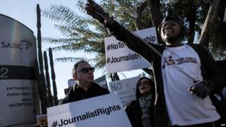 A protester in chained hands and a gas mask atop his head rallies with others outside the offices of South Africa's public broadcaster on July 1, 2016 in Johannesburg to protest against alleged bias and self-censorship in news coverage ahead of key municipal elections.