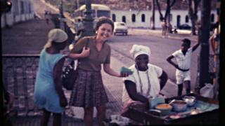 Em foto antiga, mulher aparece sorrindo ao lado de vendedora de quitutes baianos na rua