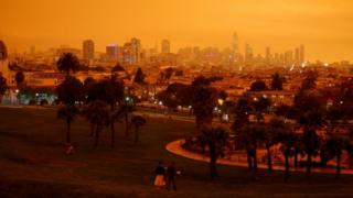 Downtown San Francisco is seen from Dolores Park under an orange sky