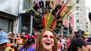 A carnival-goer wears a headdress decorated with the phrase "Love and Resistance"