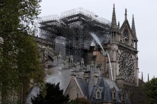 Firefighters spray water as they work to extinguish a fire at Notre-Dame Cathedral in Paris