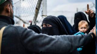 A member of the Syrian Democratic Forces (SDF) stands before veiled women at al-Hol camp