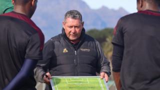 Steve Barker instructs players using a tactics board during a training session in front of a mountainous backdrop