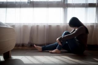 Imagem mostra mulher cabisbaixa, sentada no chão de uma casa