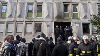 Firefighters and migrants outside a migrant reception centre in Boulogne-Billancourt, west of Paris, on 16 December 2016 after a fire broke out