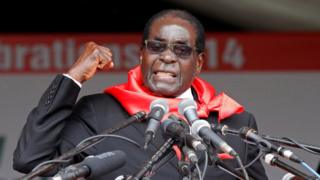 Robert Mugabe raises a fist while delivering a speech from a podium