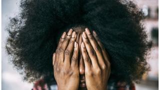 A black woman covers her face with her hands