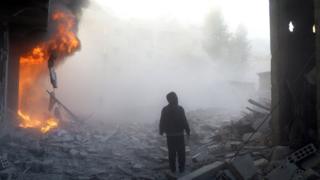 A man walks near a building on fire following a reported air strike by government forces in the rebel-held region of Eastern Ghouta, on the outskirts of the Syrian capital Damascus