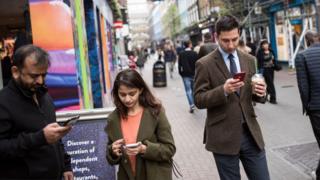 Members of the public check their mobile phones as they stand on Carnaby Street in London, on March 28, 2017.