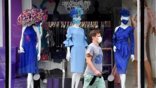 A man walking past a shop window where the mannequins have been dressed in face masks.