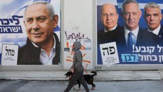 Мужчина гуляет со своей собакой между рекламными щитами предвыборной кампании премьер-министра Биньямина Нетаньяху (слева) и лидеров партии «Синий и белый» Бенни Ганца (2-R) и Яира Лапида (3-R) и Моше Яалона (R), в Тель-Авиве, Израиль, 3 апреля 2019 года