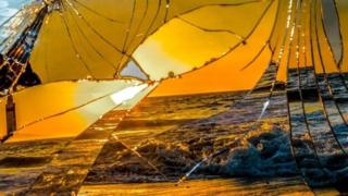 Un espejo roto refleja la imagen de una playa al atardecer.