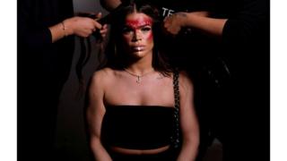 A model is seen sitting whilst her hair is styled