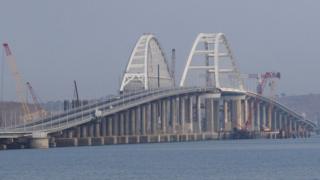 This photo shows the Kerch bridge, with some cranes along its edges, in daylight