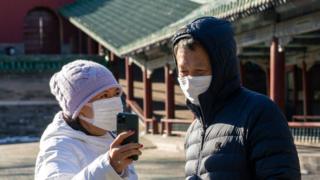 Two people in face masks look at a mobile phone