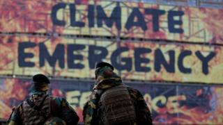 Two soldiers look at a group of activists of the environmental NGO Greenpeace taking part in a protest action after attaching a banner on the frontage of the European Council building, in Brussels