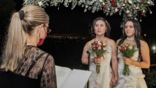 Alexandra Quiros (C) and Dunia Araya (R) stand before a lawyer during their wedding in Heredia, Costa Rica, on May 26, 2020