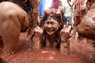 A reveller is pelted with tomatoes as she sits in a smashed tomato puree puddle at the annual Tomatina festival in Bunol, Spain