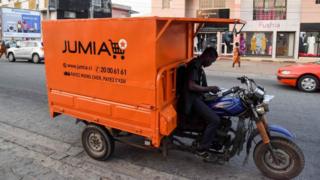 Un livreur regarde son téléphone assis sur un transporteur avec une publicité pour le site de commerce électronique nigérian Jumia à Abidjan.