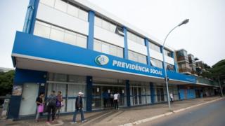 Pedestres caminham em frente a fachada de agência do INSS