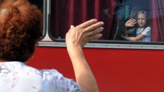Женщина машет рукой своей семье, уежающей на автобусе в Россию из Донецка в июле 2014 года