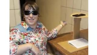 Foto de uma mulher que usa óculos escuros. Ao lado direito, uma mesa com um caderno e um suporte de madeira