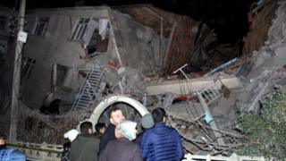 People stand outside collapsed building - 24 January