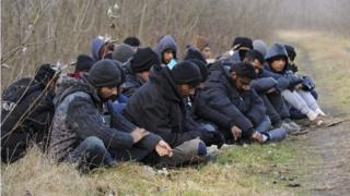 Задержанные мигранты, прибывшие через Сербию, сидят возле пограничной деревни Рошке, Венгрия, 9 февраля 2016 года