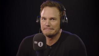 Actor Chris Pratt looks confused and shrugs at the camera in a radio stufio