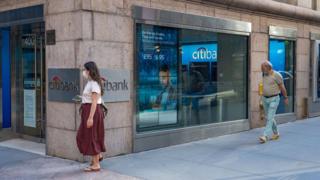 People in masks walk past a Citi ATM