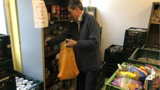 Волонтер наполняет пакет едой