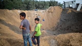 Palestinian children stand next to a crater on 22 August 2016 in Beit Lahia in the northern Gaza Strip