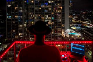 Ein Musik-DJ steht auf einem Balkon und tritt in den umliegenden Wohnungen auf
