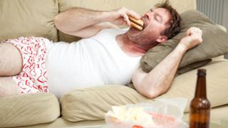 Divanda yatan adam hamburger yeyir