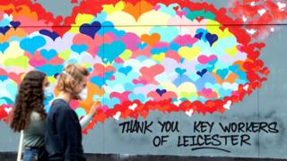 Two women walk past a mural in Leicester