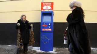 Пожилая женщина, продающая грибы на улице в Москве, а молодая женщина прогуливается по