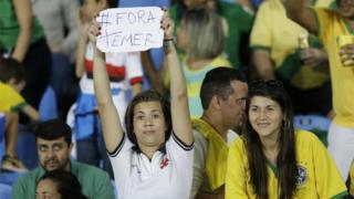 A fan in the stands holds a sign that reads in Portuguese "Temer Out" prior a group E match of the women's Olympic football tournament between Brazil and Sweden at the Rio Olympic Stadium in Rio De Janeiro, Brazil, Saturday, Aug. 6, 2016.